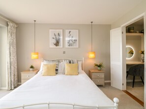 Un dormitorio con una cama grande, dos mesitas de noche, una mesilla y un espejo, con una puerta que da a un baño.