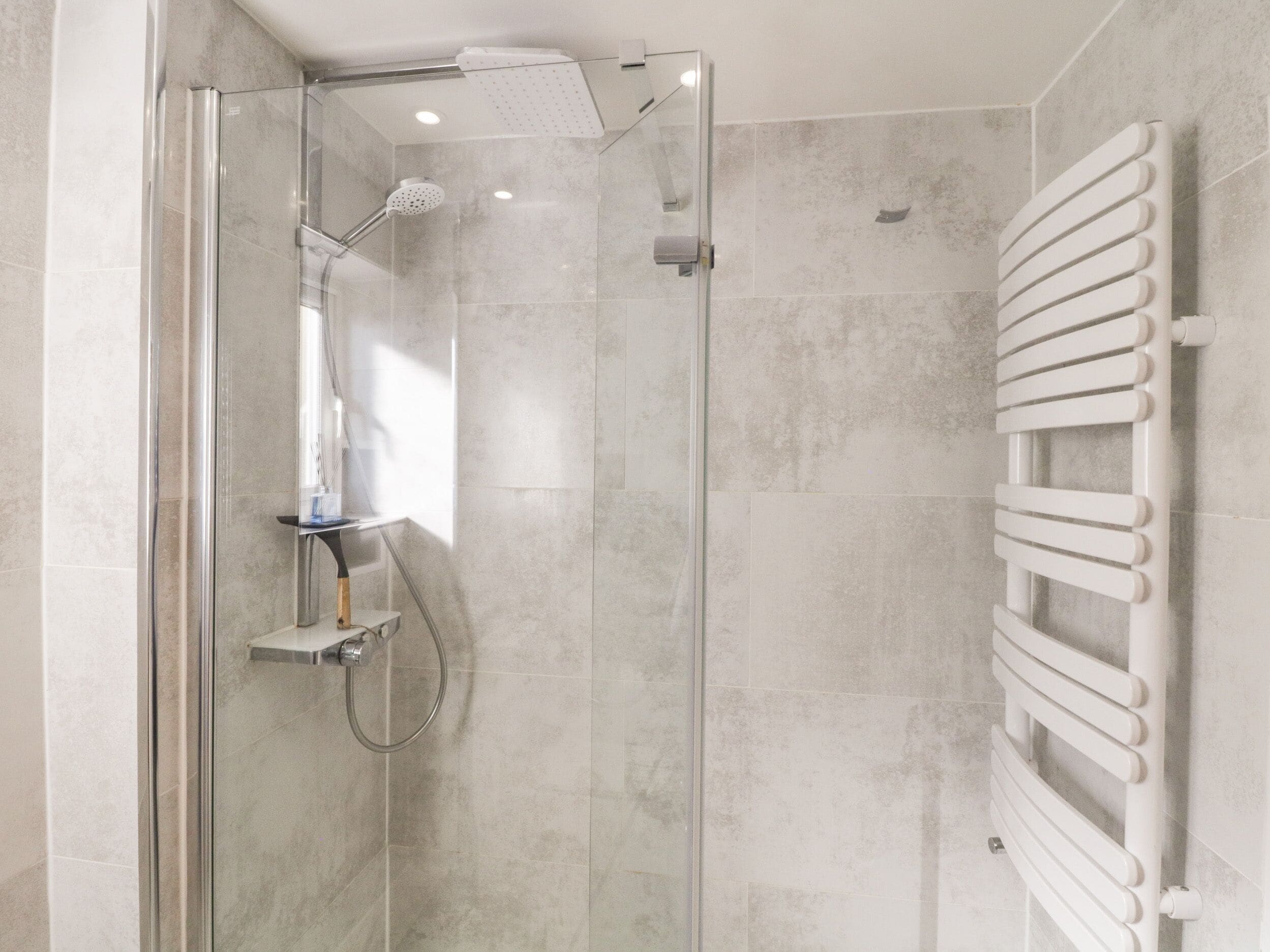 A modern shower with a glass door, a handheld showerhead, and a wall-mounted towel rail.