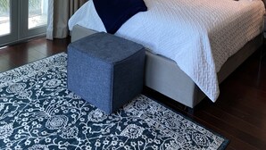 A bedroom with a large bed, a nightstand, a lamp, and a view of palm trees through a sliding door.