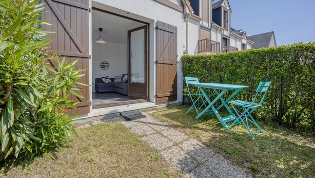 A residential property with a patio area featuring a table and chairs, a sliding door entrance, and a small seating area with cushions.