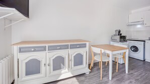 A compact kitchen with a built-in microwave, a washing machine, and a small dining table with chairs.
