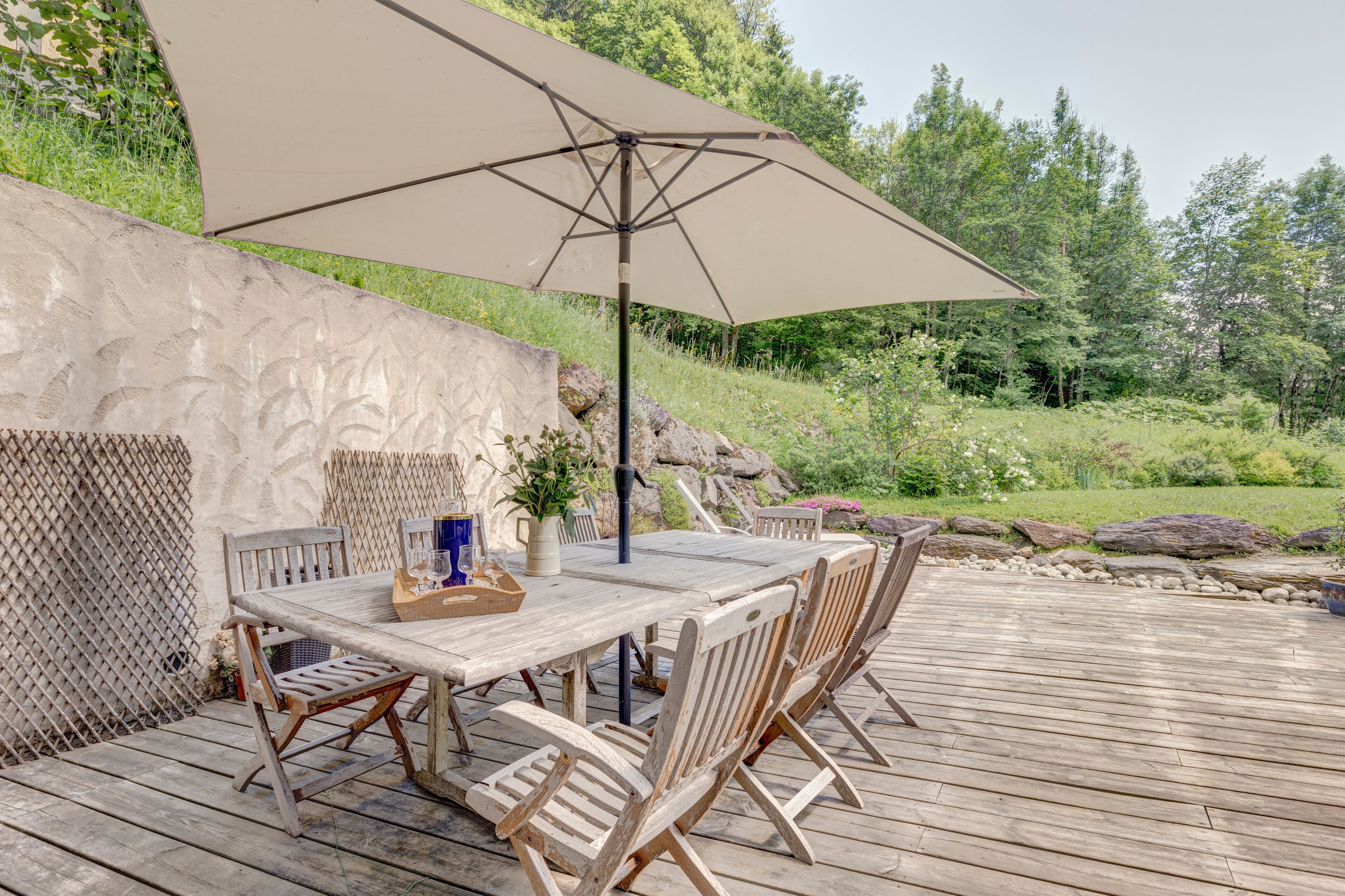 Une terrasse en bois avec une table et des chaises, un parasol beige et une plante en pot.
