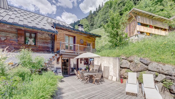 Eine Holzhütte mit einem Balkon, einer Terrasse mit Stühlen und einer Steinsäule.