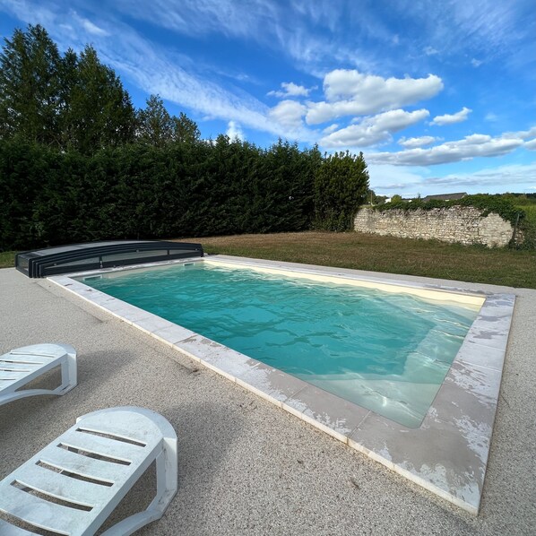 A rectangular swimming pool with a stone edge, surrounded by a gravel area. There are two white lounge chairs.