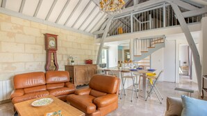 Un vaste espace de vie doté d’un haut plafond, d’une table à manger, d’un canapé et d’un escalier menant à un niveau supérieur.