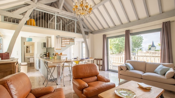 Un vaste espace de vie doté d’un haut plafond, d’une table à manger, de canapés en cuir et offrant une vue sur l’extérieur.