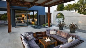 An outdoor seating area with a fire feature, a modern building with large windows, and a stone structure.