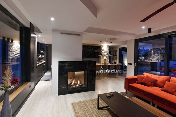 A modern living room with a fireplace, a sofa, and a dining area with a table and chairs.