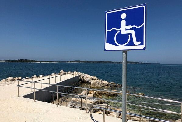 Señal de accesibilidad para sillas de ruedas junto a un paseo marítimo.