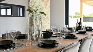 A dining table set with black plates, silverware, and clear glasses, with a vase of white flowers in the center.