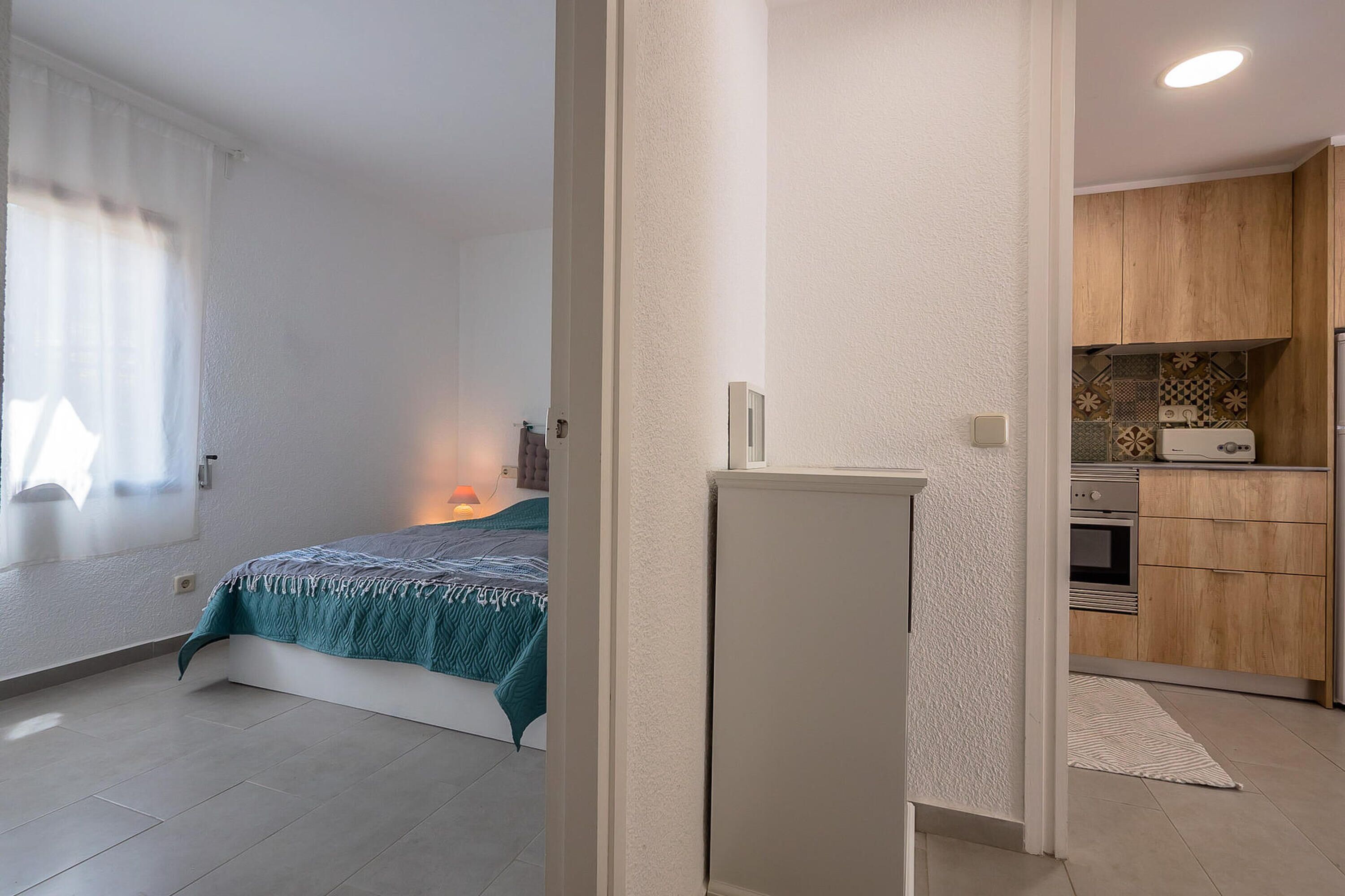 A bedroom with a bed, a bedside table, and a nightstand. There is a window with curtains and a view of the outside.