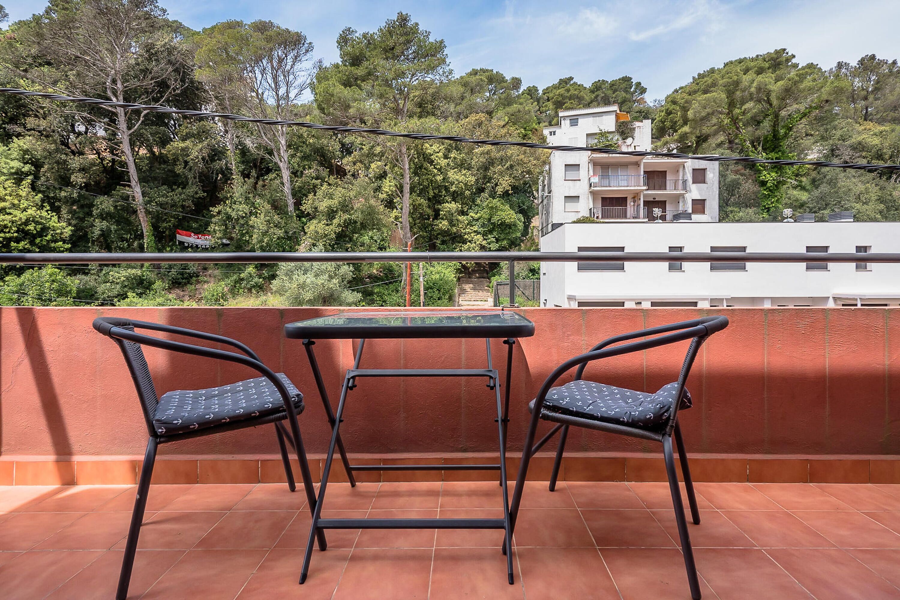 Een balkon met twee stoelen en een tafel, met uitzicht op een woonwijk met bomen en gebouwen.