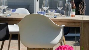 An outdoor dining area with a table set for two, chairs, and a potted plant with pink flowers. - Raaff-71 sfeervol huis direct bij bos, duin en strand (Noordwijk)