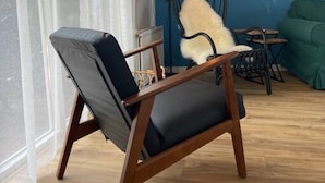 A room with a wooden floor, a blue wall, a black chair with a white cushion, a table with chairs, and a floor lamp. - Raaff-71 sfeervol huis direct bij bos, duin en strand (Noordwijk)