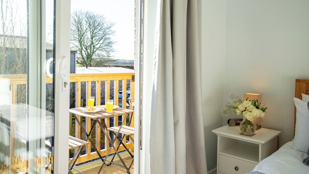 Une chambre avec vue sur une terrasse en bois et une table sur laquelle se trouve un verre de jus d’orange.