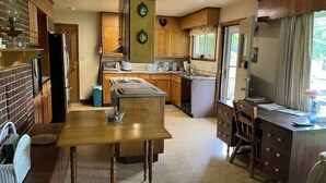 Een keuken met houten kastjes, een centraal eiland, een eettafel en een klein werkgedeelte met een bureau en stoel.