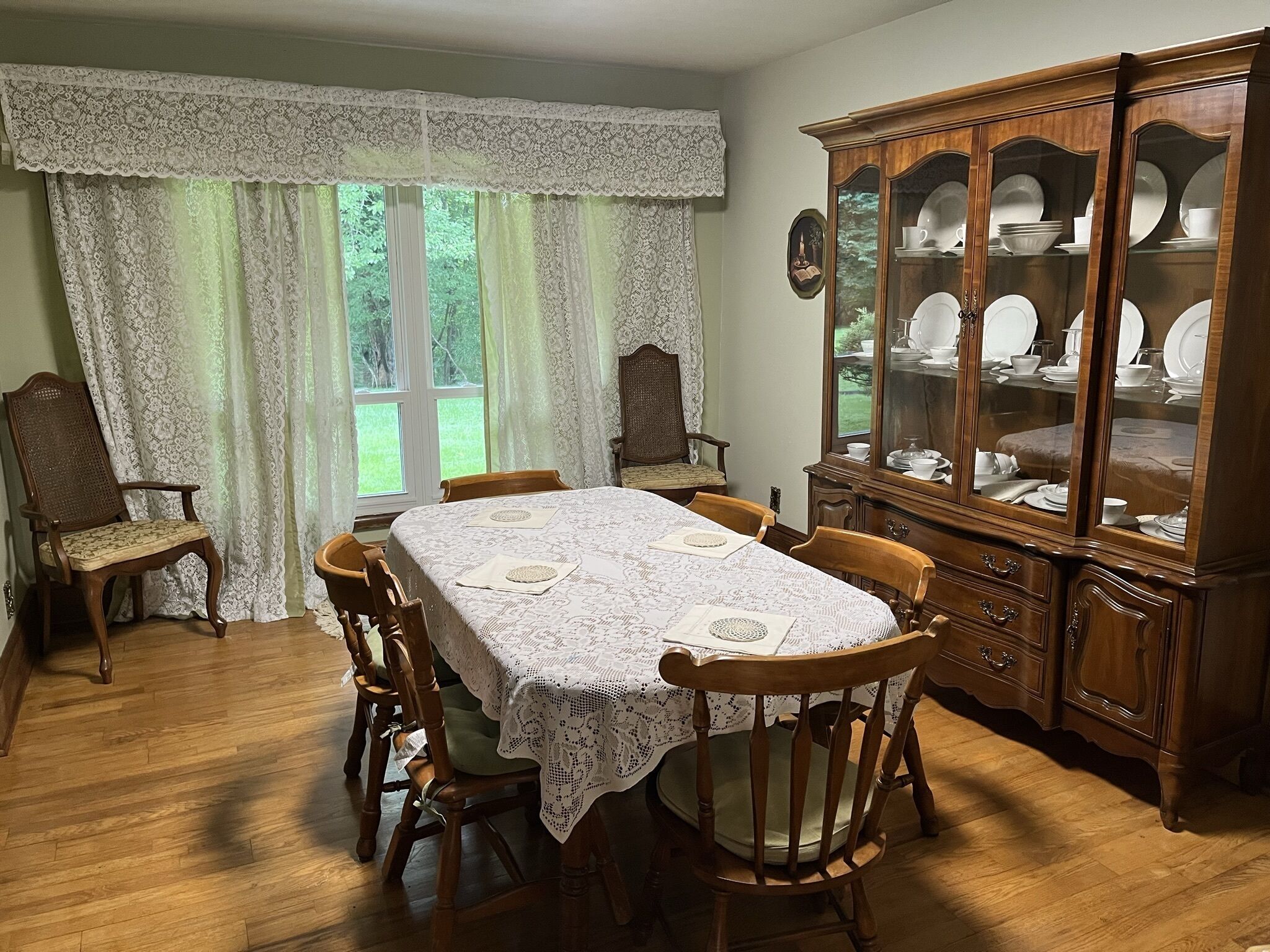 Comedor con mesa de madera, sillas, cortinas de encaje y aparador.