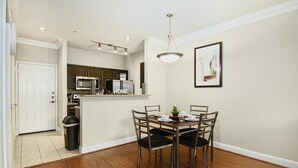 Un coin repas avec une table et des chaises en bois, une cuisine en arrière-plan et un tableau encadré au mur.