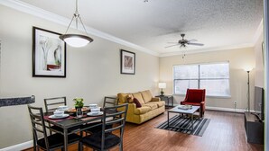Un coin repas avec une table dressée pour quatre personnes, un canapé, un fauteuil rouge et un ventilateur de plafond.