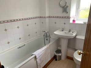 Un baño con bañera, lavamanos, inodoro y ventana con vistas al verdor.