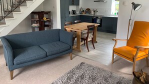 Een woonkamer met een blauwe bank, een houten eettafel met stoelen, een trap met zwarte leuningen, en een keuken op de achtergrond.