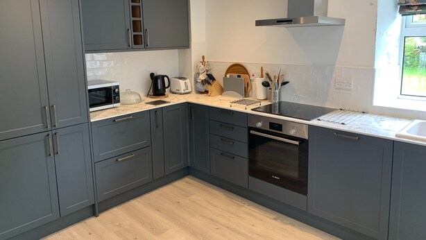 Een moderne keuken met grijze kastjes, een ingebouwde oven en een raam dat voor natuurlijk licht zorgt.