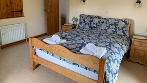 Een slaapkamer met een houten bed, een radiator, een houten kledingkast en een nachtkastje met een lamp.
