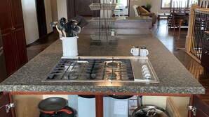 Une cuisine dotée d’un plan de travail en granit, d’une cuisinière à gaz et de divers ustensiles de cuisine. Un luminaire est suspendu au-dessus de la cuisinière.