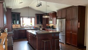 Une cuisine spacieuse avec des meubles de couleur bois foncé, un grand îlot central doté de tabourets, un réfrigérateur en acier inoxydable et un luminaire suspendu.