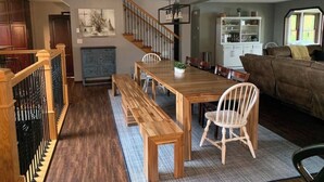 Un grand espace à manger avec une table et des bancs en bois, un escalier et un salon doté d’un canapé.
