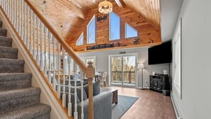 A spacious living area with a staircase, a fireplace, and a large window overlooking a deck. - Deer Crossing Retreat - new home close to Saddleback (Dallas Plantation)