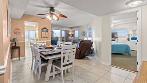 Un comedor con una mesa y sillas, un ventilador de techo, y vista a una sala de estar con un sofá y una cama.