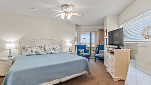 Habitación de hotel con cama, televisor, ventilador de techo y vistas al exterior.