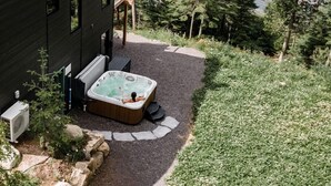 Una cabaña moderna con hidromasaje, rodeada de un bosque y un lago.