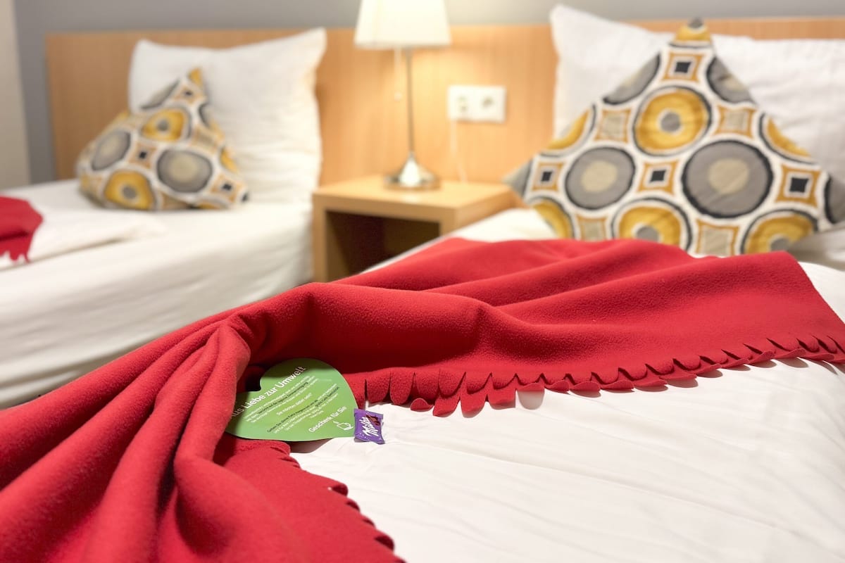 Une chambre d’hôtel avec deux lits, chacun agrémenté d’oreillers à motifs et d’une couverture rouge.