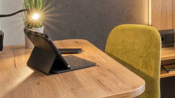 A wooden table with a laptop on a stand, a green chair, and a potted plant with a light source behind it.