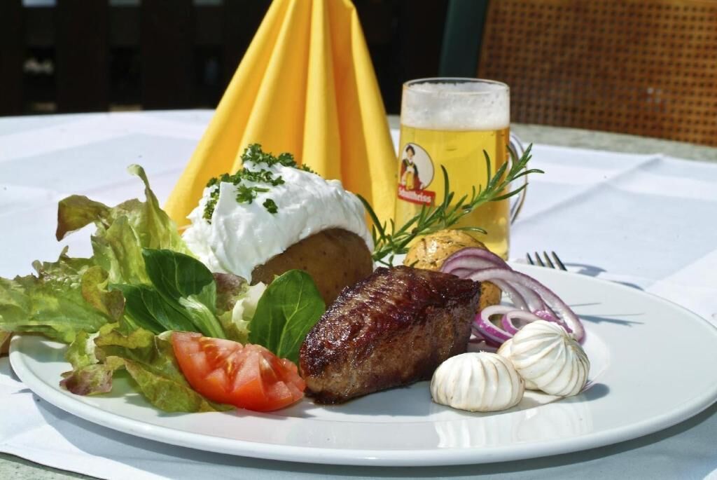 Ein Teller mit einem Steak, Salat und Knoblauch, dazu ein Bier und ein gelber Kegel.