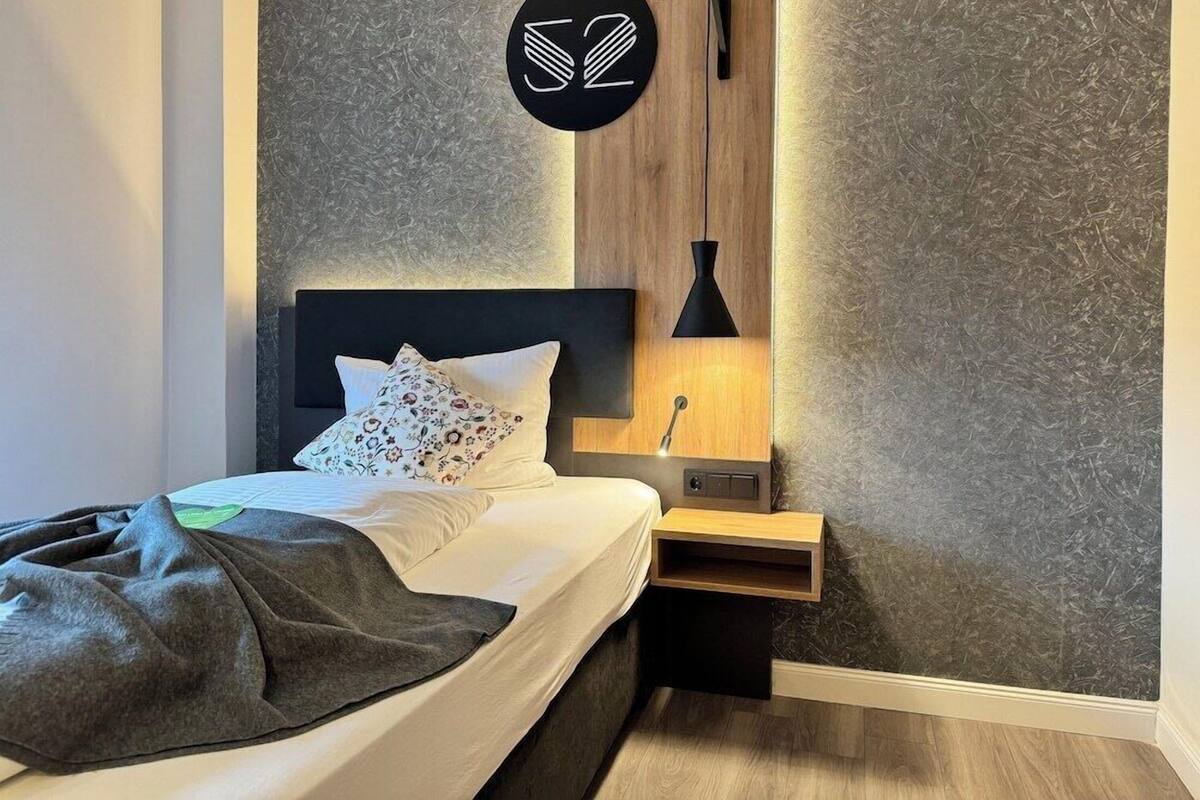 Une chambre à coucher moderne avec un lit, une table de chevet, une lampe fixée au mur et un panneau décoratif avec un numéro.