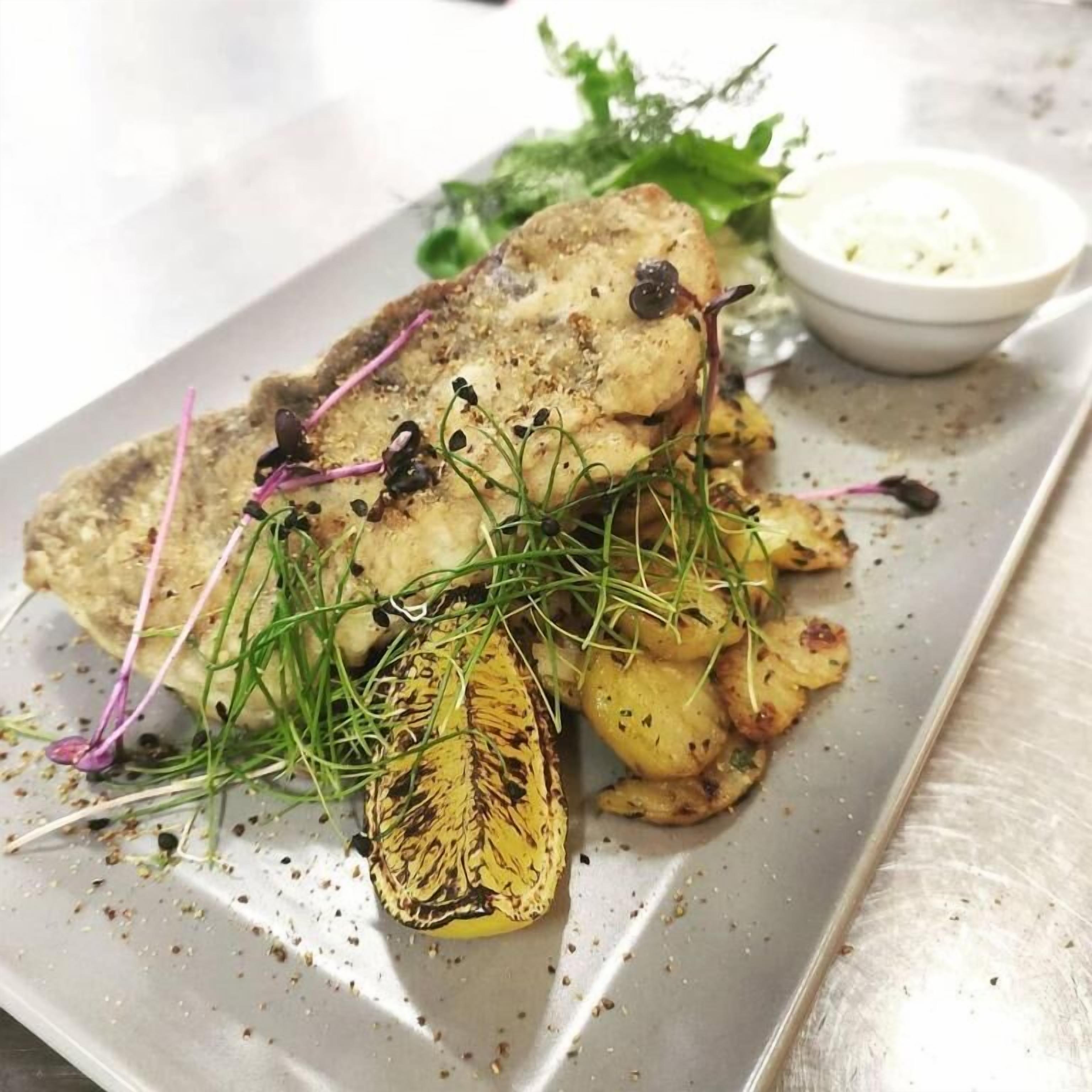 A plated dish with roasted potatoes, greens, and a small bowl of sauce.