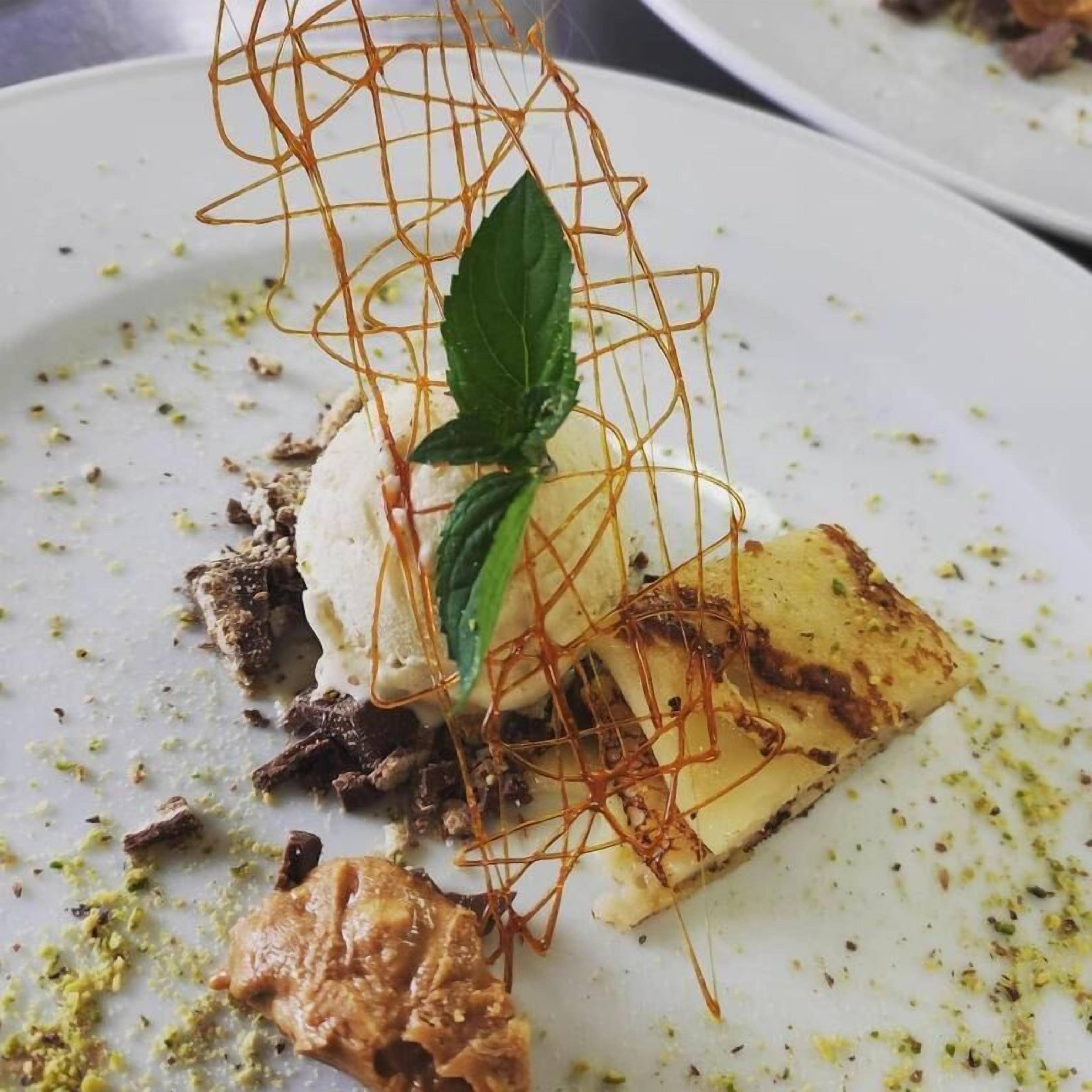 A dessert plate with a wire structure, ice cream, mint leaf, and a piece of cake.