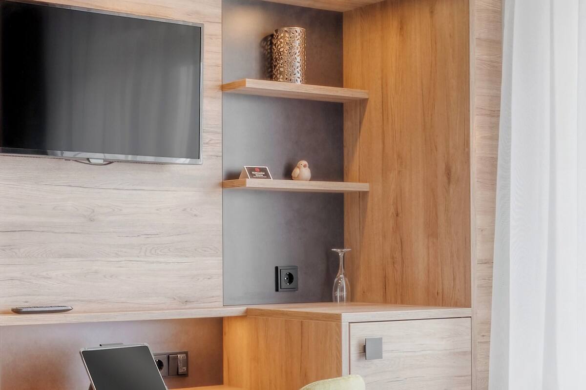 Une chambre d’hôtel moderne dotée d’un bureau en bois, d’un téléviseur à écran plat, d’un lit et d’un petit coin salon.