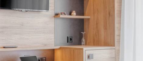 A modern hotel room with a wooden desk, a flat-screen TV, a bed, and a small seating area.