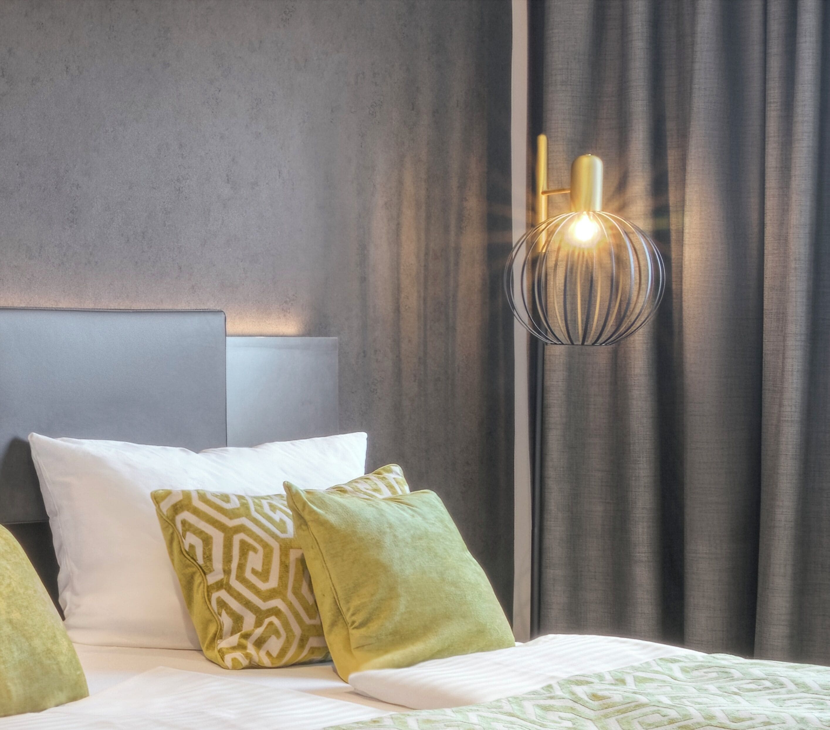 A modern bedroom with a bed, pillows, and a wall-mounted light fixture.