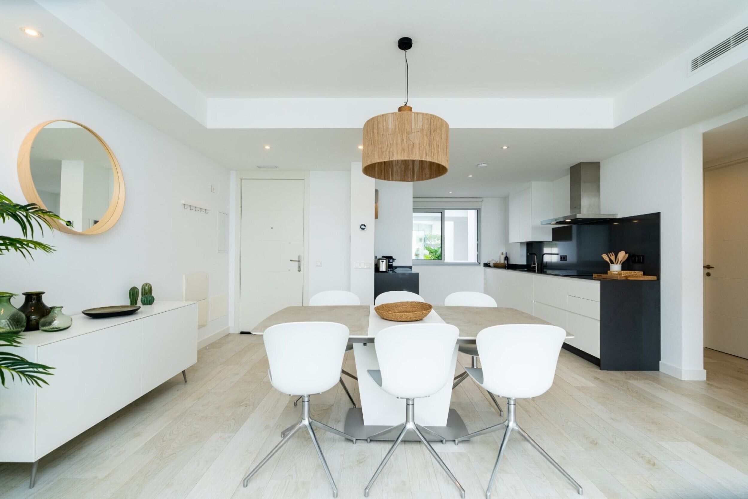 A modern kitchen with white cabinets, a central island, and a dining area with white chairs.