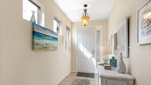 A hallway with a white door, a painting, a lamp, and a mirror on the wall.