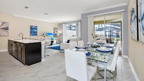 A modern kitchen with a central island, a dining area with a glass table, and a living space with a sofa and coffee table. - Amazing Story Lake Town Home  With Pool (Kissimmee)