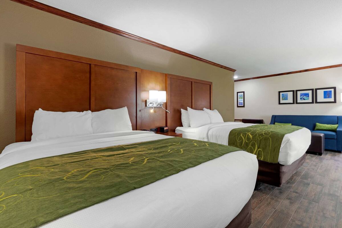 A hotel room with two beds, a blue sofa, and a wooden headboard.
