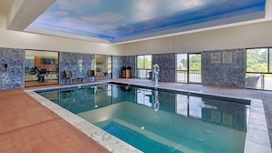 Una piscina interior con un mural en el techo, ventanas amplias y una pared de piedra con un cartel de 'No Diving'.