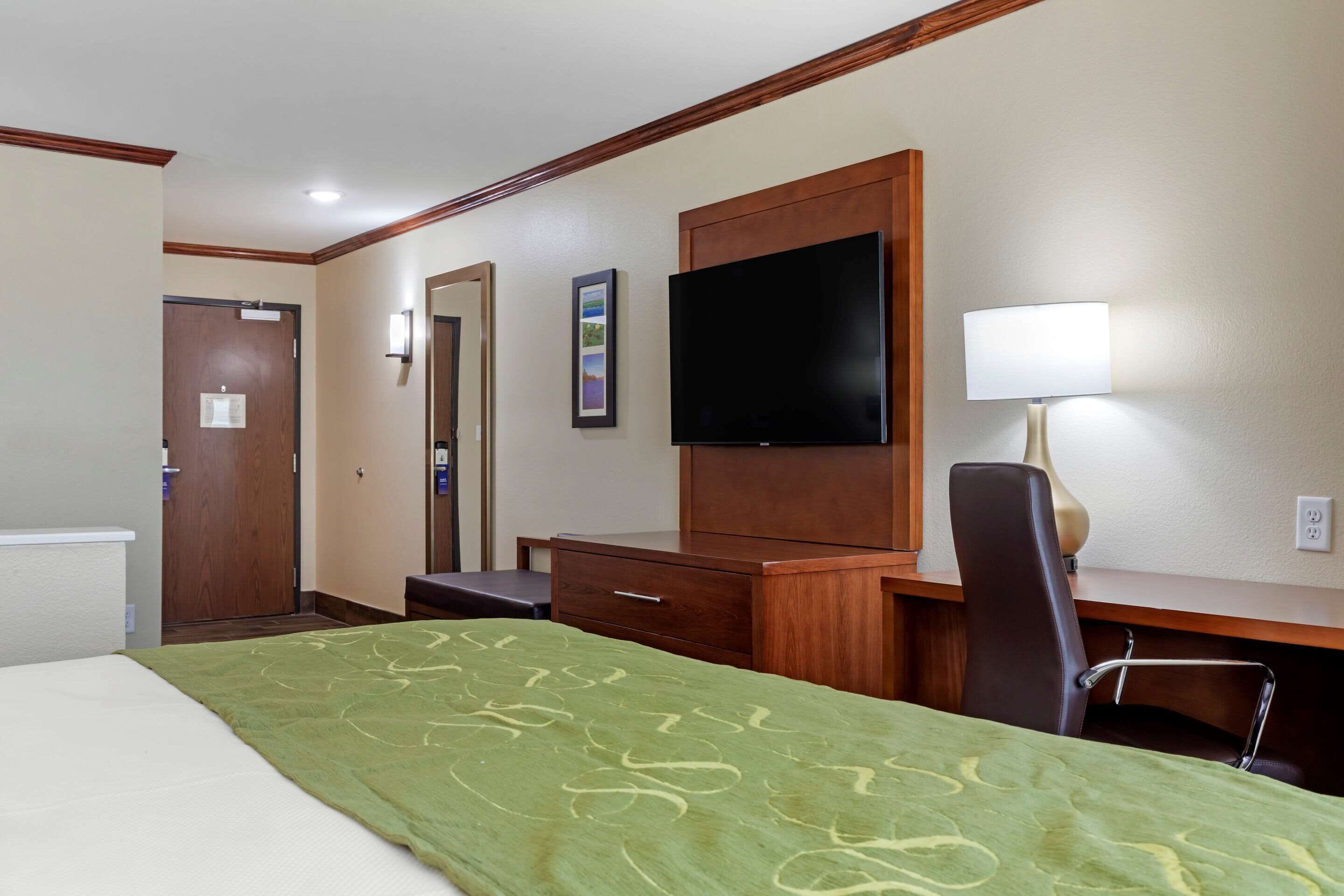 A hotel room with a bed, a desk, a chair, a television, and a lamp.