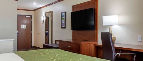 A hotel room with a bed, a desk, a chair, a television, and a lamp.